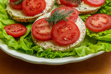 dietetic crispbreads with cream cheese and tomato slices on lettuce leaves on a plate, healthy lifestyle concept
