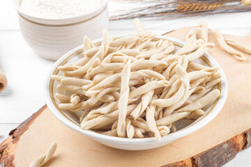 Whole grain wheat raw apulian pasta called Pizzarieddi or maccaruni on a ceramic plate on white wooden table. Fresh maccheroni typical dish of Puglia, Salento Italy. Italian homemade pasta background