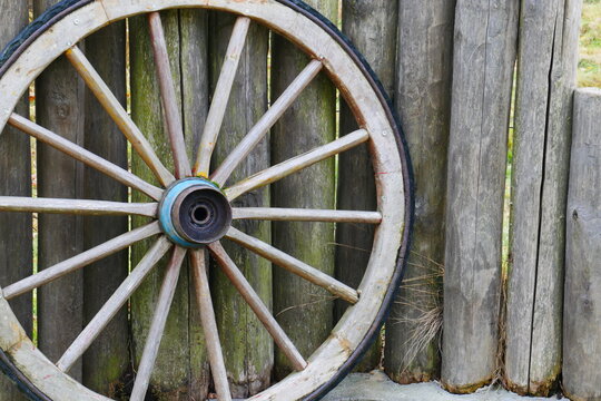 an old wooden wagon wheel from the wild west stands on a fence made of wooden stakes