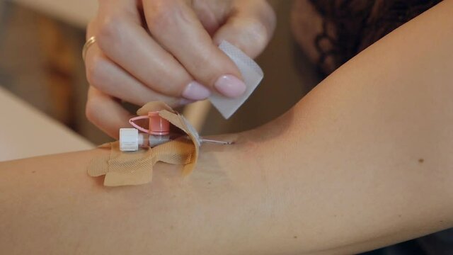 Female hands with a catheter on a vein for injection, rubbing the blood. Home treatment