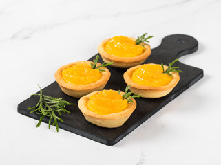 Dessert mini Tartlets with custard and slices of tangerines covered with syrup on a serving board on a white background