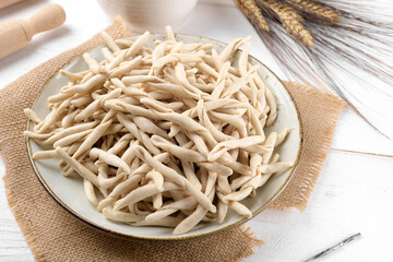 Whole grain wheat raw apulian pasta called Pizzarieddi or maccaruni on a ceramic plate on white wooden table. Fresh maccheroni typical dish of Puglia, Salento Italy. Italian homemade pasta background