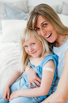 Mother and daughter laugh into the camera with fresh vaccination and plaster.
