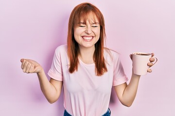 Redhead young woman drinking a cup coffee screaming proud, celebrating victory and success very excited with raised arm