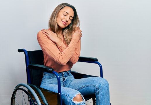 Beautiful hispanic woman sitting on wheelchair hugging oneself happy and positive, smiling confident. self love and self care