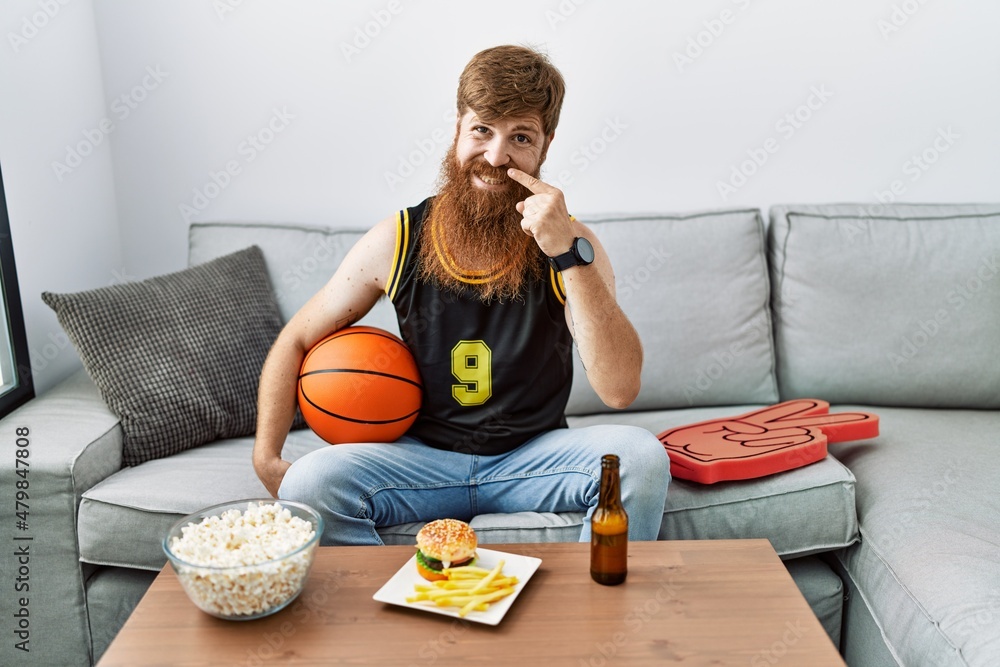 Poster caucasian man with long beard holding basketball ball cheering tv game pointing with hand finger to 