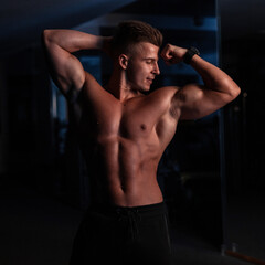 Fototapeta na wymiar Handsome young sports man with a sexy naked torso and muscles in the gym on a dark background