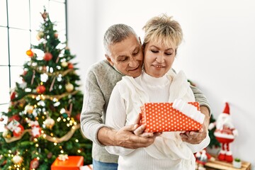 Obraz na płótnie Canvas Middle age caucasian couple smiling happy holding christmas gift at home.