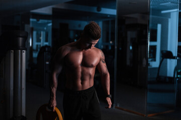 Fototapeta na wymiar Sport. Young athletic man doing workout in the dark. Muscular and strong guy exercising.