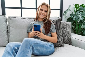 Obraz premium Young caucasian girl using smartphone sitting on the sofa at home.