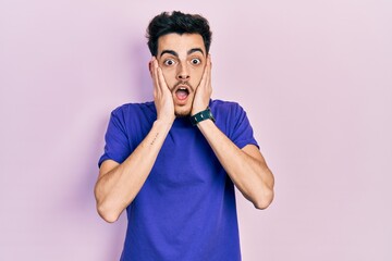 Young hispanic man wearing casual t shirt afraid and shocked, surprise and amazed expression with hands on face
