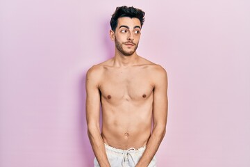 Fototapeta premium Young hispanic man wearing swimwear shirtless smiling looking to the side and staring away thinking.
