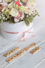 Flowers in a round box on a light wooden background and the inscription Happy Valentine's Day