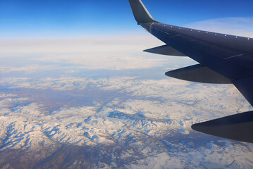 Obraz premium View to the wing of airplane in the sky and snowy mountains. Travel and transportation concept