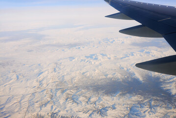 Fototapeta na wymiar View to the wing of airplane in the sky and snowy mountains. Travel and transportation concept