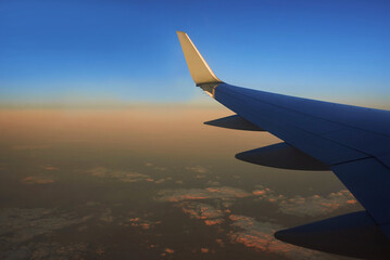 Obraz premium View to the wing of airplane in the sky during sunset. Travel and transportation concept