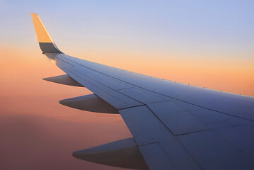 Plakat View to the wing of airplane in the sky during sunset. Travel and transportation concept