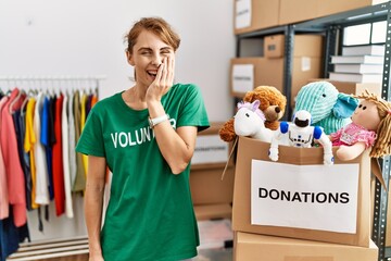 Beautiful caucasian woman wearing volunteer t shirt at donations stand laughing and embarrassed...