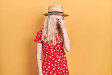Beautiful caucasian woman with blond hair wearing summer hat tired rubbing nose and eyes feeling fatigue and headache. stress and frustration concept.