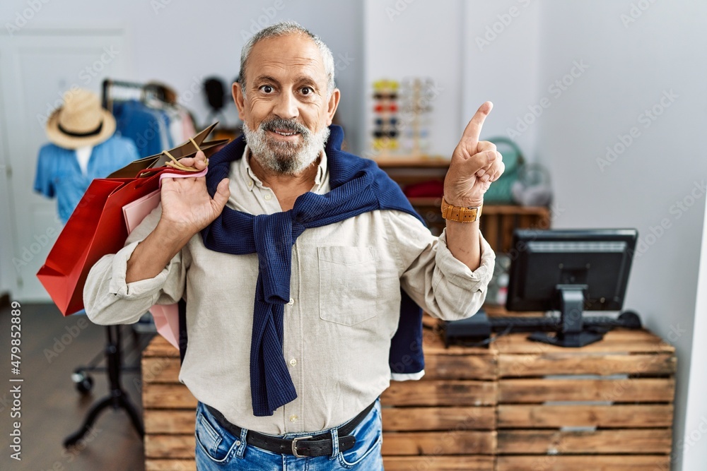 Sticker handsome senior man holding shopping bags at boutique shop with a big smile on face, pointing with h