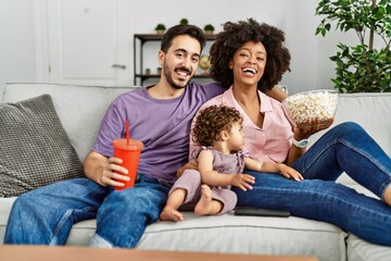 Couple and daughter watching movie sitting on sofa at home