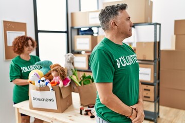 Middle age man wearing volunteer t shirt at donations stand looking to side, relax profile pose with natural face with confident smile.