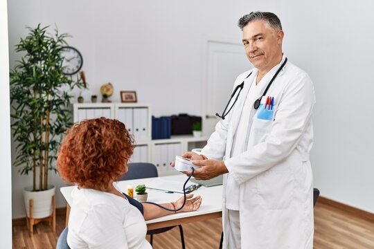 Middle age man and woman wearing doctor uniform using tensiometer having medical consultation at clinic