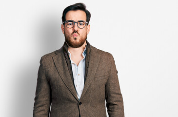 Young hispanic man wearing business jacket and glasses making fish face with lips, crazy and comical gesture. funny expression.