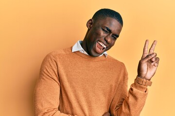 Young african american man wearing casual clothes smiling with happy face winking at the camera doing victory sign. number two.