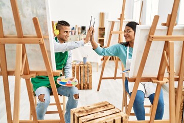 Young latin painter couple high five painting and using headphones at art studio