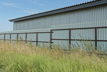 large gray metal industrial building an iron fence in green grass against the sky