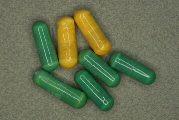 a pile of yellow and green medical capsules of pills lie on a gray table