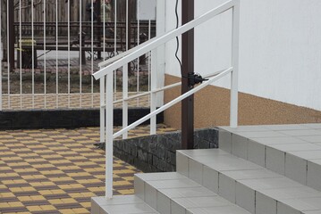 gray stone steps and a threshold with white metal handrails outside on a brown sidewalk