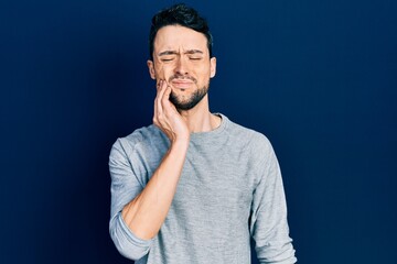 Young hispanic man wearing casual clothes touching mouth with hand with painful expression because of toothache or dental illness on teeth. dentist