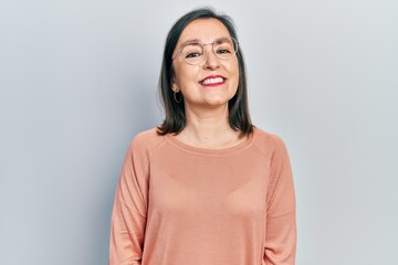 Obraz premium Middle age hispanic woman wearing casual clothes and glasses looking positive and happy standing and smiling with a confident smile showing teeth