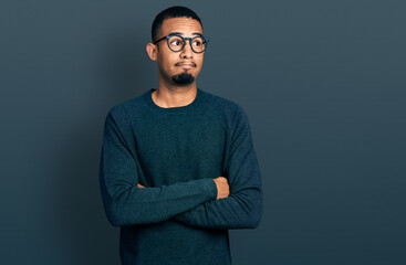 Fototapeta premium Young african american man wearing casual clothes and glasses smiling looking to the side and staring away thinking.