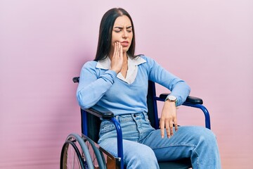 Beautiful woman with blue eyes sitting on wheelchair touching mouth with hand with painful expression because of toothache or dental illness on teeth. dentist