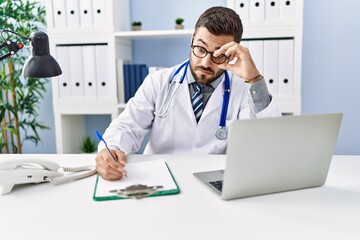 Fototapeta na wymiar Young hispanic man wearing doctor uniform stressed working at clinic
