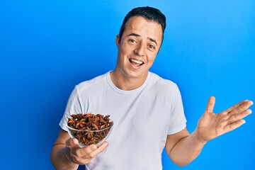 Handsome young man holding bowl of star anise celebrating achievement with happy smile and winner...