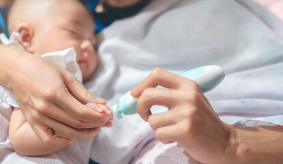 Father cutting my baby's nails with electic nail clipper while baby sleep.