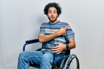 Handsome hispanic man sitting on wheelchair pointing aside worried and nervous with forefinger,...
