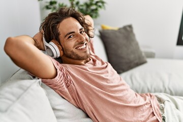 Young hispanic man relaxed with hands on head listening to music at home.
