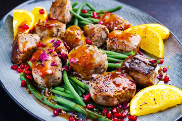 Modern style jusy seared pork pigllet tenderloin fillet meat medallions with orange relish sauce, pomegranate and green baby beans vegetable served as close-up on a Nordic design plate