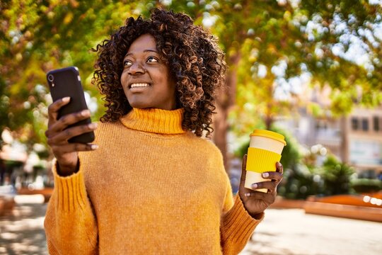 African american woman using smartphone drinking coffee at park