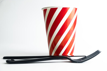 Paper cup with plastic spoon and fork on table prepared for party. Black
