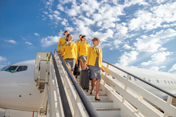 Cheerful stewardesses walking down airplane stairs under cloudy sky