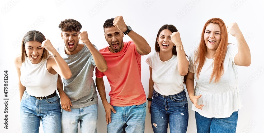 Poster group of young friends standing together over isolated background angry and mad raising fist frustra