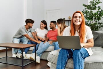 Fototapeta premium Group of young friends speaking sitting on the sofa. Woman smilimg happy and using laptop at home.