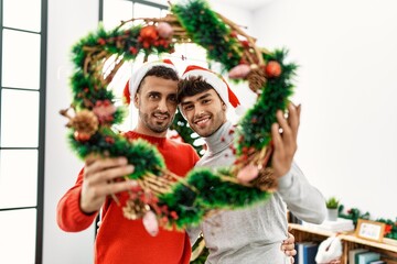 Two hispanic men couple hugging each other holding christmas decor at home