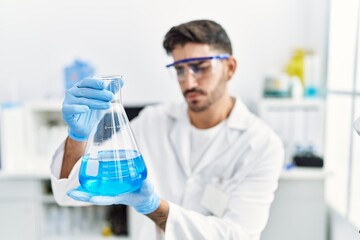 Handsome hispanic man working as scientific holding erlenmeyer flask at laboratory